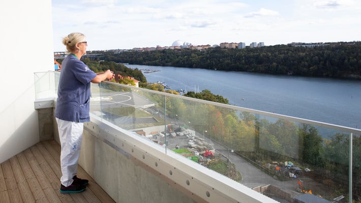 En kvinna i vårdkläder som blickar ut över Årstaviken.