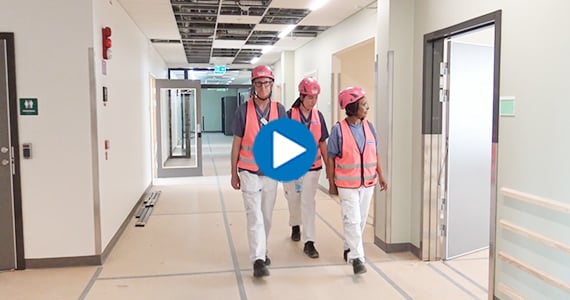 Sven Jönhagen, Elin Hansson och Messi Asfaw-Lundin med rosa hjälm och väst i korridor i ny vårdbyggnad.